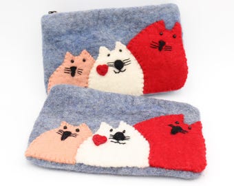 Può includere: Due pochette in feltro blu chiaro con chiusura a zip. Ogni pochette presenta tre facce di gatto applicate in rosa, bianco e rosso. Il gatto bianco ha un cuore rosso. I gatti hanno dettagli ricamati neri.