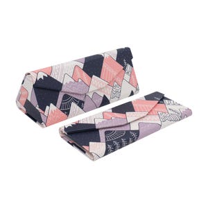 May include: Two foldable eyeglass cases with a mountain range pattern. The cases feature a design of pink, purple, and white mountains against a navy blue background. One case is open, and the other is closed.