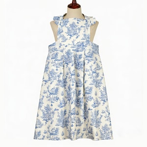 K&ouml;nnte beinhalten: Ein wei&szlig;-blaues Kleid mit Toile-de-Jouy-Druck, plissiertem Rock und R&uuml;schen-Tr&auml;gern. Das Kleid zeigt ein klassisches pastorales Szenen-Design in Blau auf wei&szlig;em Hintergrund. Das Kleid wird auf einer Schaufensterpuppe pr&auml;sentiert.
