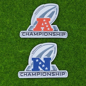 May include: Two patches with a football shape and the text "CHAMPIONSHIP". One patch has a red "A" with stars, the other has a blue "N" with stars. The patches are on a green surface.