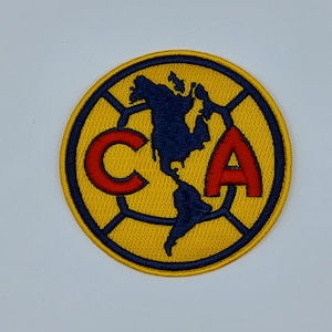 May include: A circular embroidered patch featuring a yellow background with a dark blue border. The design includes a dark blue silhouette of the North and South American continents, flanked by the red capital letters C and A on either side.