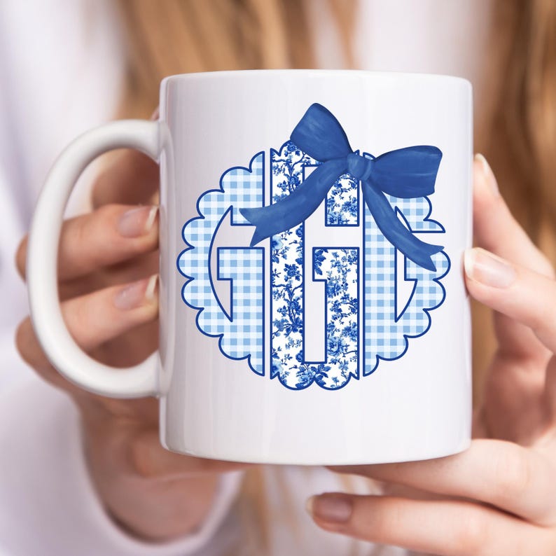 May include: White ceramic mug with a blue and white floral and gingham design and a blue bow. The design is in the shape of a cross. The mug has a curved handle.