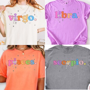 May include: Four t-shirts with colorful text and star graphics. The shirts are cream, purple, orange, and gray. The text on the shirts reads "Virgo", "Libra", "Pisces", and "Scorpio". Each shirt has a bow graphic.
