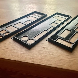 Könnte beinhalten: Drei schwarze Kunststoffplatten mit Ausschnitten für verschiedene Komponenten. Die Platten liegen auf einer hellbraunen Holzoberfläche.