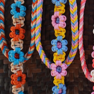 May include: Five colourful braided necklaces with flower-shaped beads. The necklaces are made of different colours of string and have a variety of flower designs.
