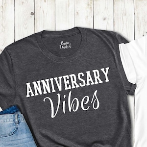 May include: Two t-shirts with the text 'Anniversary Vibes' in black on a white t-shirt and white on a gray t-shirt.