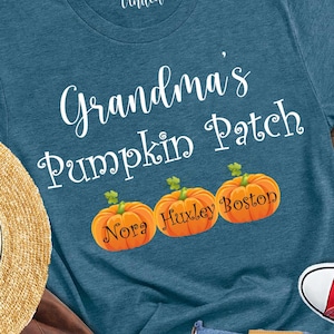 May include: A teal t-shirt with the text "Grandma's Pumpkin Patch" and three orange pumpkins. The image also includes a straw hat, brown backpack, blue jeans, and red sneakers.