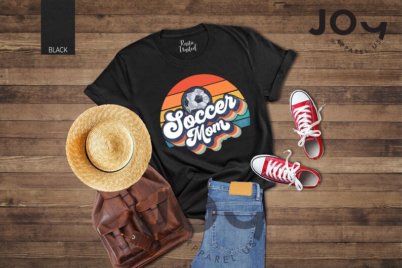 May include: Black t-shirt with a "Soccer Mom" graphic, a straw hat, a brown backpack, blue jeans, and red trainers. The shirt features a soccer ball design with a retro colour scheme.