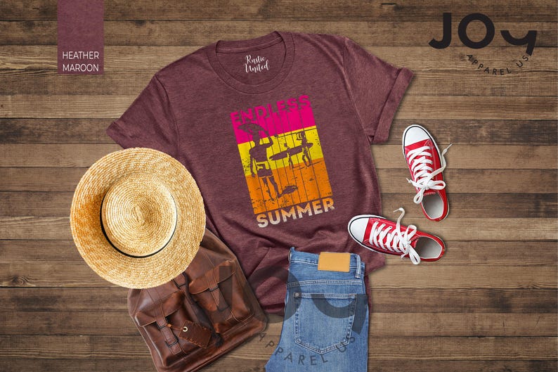 May include: A maroon t-shirt with a graphic that says "Endless Summer" with a surfer theme, red sneakers, a straw hat, a brown backpack, and blue jeans. The items are arranged on a wooden surface.