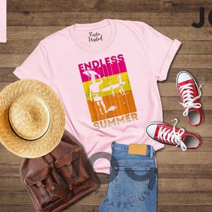 May include: A light pink t-shirt with the words "ENDLESS SUMMER" and a graphic of a person surfing. The image also includes a straw hat, brown backpack, blue jeans, and red sneakers.