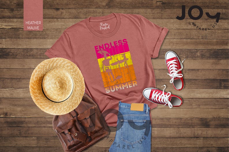 May include: A heather mauve t-shirt with the words "ENDLESS SUMMER" in a colorful graphic, paired with red sneakers, blue jeans, a straw hat, and a brown leather backpack. The items are arranged on a wooden surface.