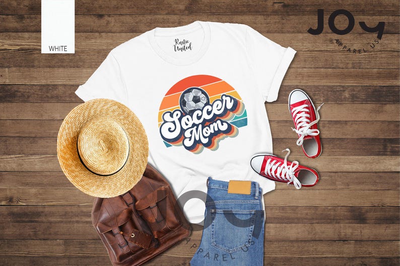 May include: A white t-shirt with a retro "Soccer Mom" design and a soccer ball graphic. The image includes red trainers, blue jeans, a straw hat, and a brown backpack. The shirt is from Joy Apparel US.