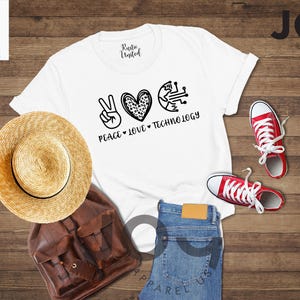 May include: White t-shirt with the words "PEACE LOVE TECHNOLOGY" and graphics of a peace sign, a heart, and a circuit board. The image also includes red sneakers, a straw hat, a brown backpack, and blue jeans.