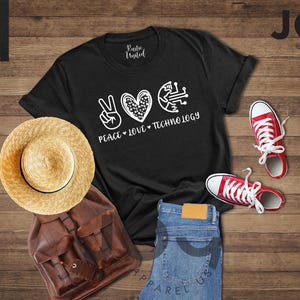 May include: Black t-shirt with the words "Peace Love Technology" in white, along with a peace sign, heart, and circuit board graphic. The image includes red sneakers, a straw hat, a brown backpack, and blue jeans.