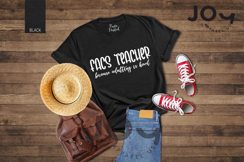 May include: Black t-shirt with the text "FACS TEACHER because adulting is hard" in white. The image includes a straw hat, brown leather backpack, blue jeans, and red sneakers with white laces. The items are arranged on a wooden surface.