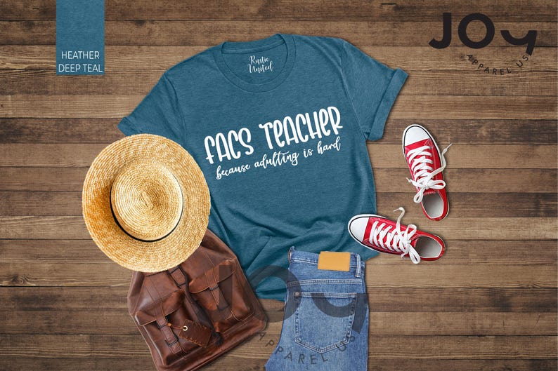 May include: A teal t-shirt with the text "FACS TEACHER because adulting is hard" is displayed with a straw hat, brown backpack, blue jeans, and red sneakers. The items are arranged on a wooden surface.