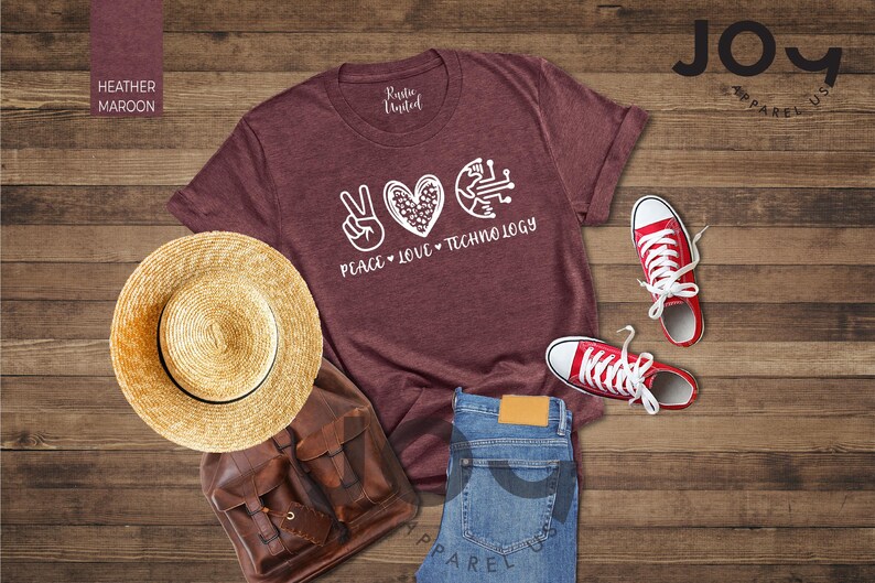 May include: A heather maroon t-shirt with the words "Peace, Love, Technology" and a peace sign, heart, and circuit board graphic. The image includes red sneakers, blue jeans, a straw hat, and a brown backpack.