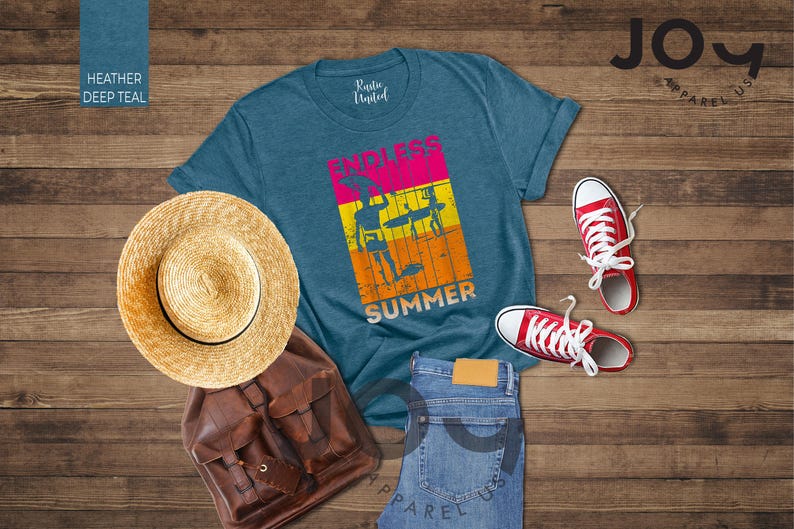 May include: A teal t-shirt with "ENDLESS SUMMER" text and graphic, straw hat, brown backpack, blue jeans, and red sneakers on a wood background. The shirt has a retro design with surfers. A casual summer outfit.