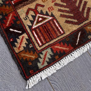 Pu&ograve; includere: Primo piano di un tappeto marrone, rosso e crema con un motivo geometrico. Il tappeto ha un bordo a frangia.