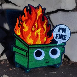 May include: A green, cartoon-style dumpster with googly eyes and a smiling mouth is on fire. A speech bubble above the dumpster says "I'm Fine".