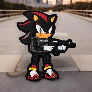 May include: A black and red cartoon character, Shadow the Hedgehog, is holding a black rifle. He is wearing a black tactical vest with the word "SHADOW" printed on it. The character is standing on a gray surface.