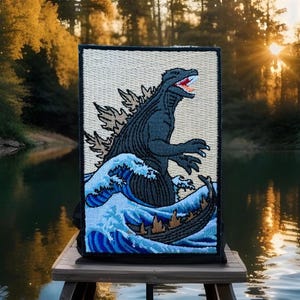 May include: Embroidered patch featuring a black Godzilla monster emerging from a blue wave, reminiscent of the Great Wave off Kanagawa artwork. The patch has a beige background and black border.