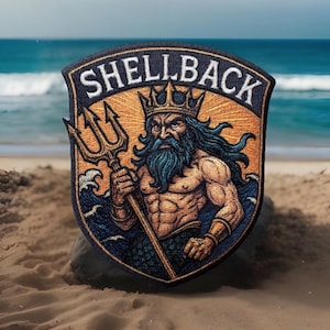 May include: Embroidered patch featuring a muscular, bearded figure with a crown, holding a trident. The patch reads "SHELLBACK" in white letters on a navy blue shield-shaped background, with a gold and blue color scheme.