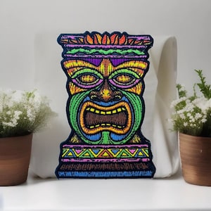 May include: Embroidered patch featuring a colorful Tiki mask design. The patch showcases a vibrant array of colors including green, yellow, purple, and orange, with a detailed, open-mouthed expression. The patch is likely for clothing or accessories.