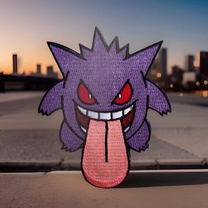 May include: Embroidered purple patch featuring a cartoon ghost with red eyes and a long pink tongue. The patch has a jagged head and a wide, toothy grin. The background shows a city skyline at dusk.