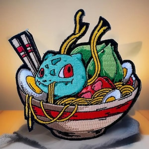 May include: A blue and green cartoon character with red eyes is sitting in a bowl of ramen noodles. The character is holding chopsticks and has a piece of seaweed in its mouth. The bowl is decorated with red and white stripes.