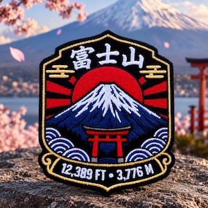 May include: A shield-shaped embroidered patch featuring a snow-capped mountain, a red sun, and a red torii gate. The text reads 富士山, 12,389 FT, and 3,776 M. The design includes blue waves, gold accents, and a black border on a dark fabric background.