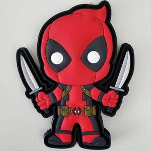 May include: A red and black cartoon Deadpool character with two silver knives. The character is wearing a red and black suit with a brown belt and pouches. The character is holding a knife in each hand.