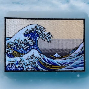 May include: Embroidered patch featuring a blue and white wave with a mountain in the background. The wave is depicted in the style of the famous Japanese woodblock print "The Great Wave off Kanagawa" by Katsushika Hokusai.
