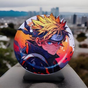 May include: A round, white, fabric-covered phone stand with a colorful anime character printed on it. The character has spiky blond hair, blue eyes, and is wearing a black and blue outfit. The background is a blurred image of a city skyline.