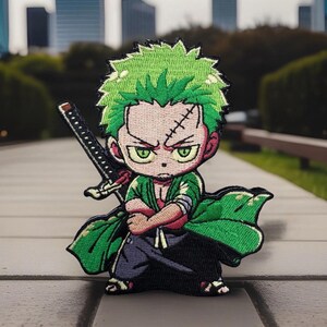 May include: A green and black embroidered patch of a cartoon character with green hair, a scar on his forehead, and a sword. The character is wearing a green and black outfit and is holding a sword.