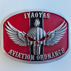 May include: Oval metal belt buckle with a red background and silver trim. The buckle features a skull with wings and the American flag design. The text "IYAOYAS" and "AVIATION ORDNANCE" are displayed.
