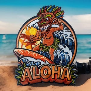May include: An embroidered patch featuring a cartoon tiki surfing on a wave with a sunset and palm trees in the background. The text "ALOHA" is written in orange and yellow letters below the image.