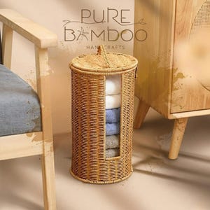 May include: A cylindrical woven bamboo storage basket with a lid and a rectangular opening revealing folded towels. The towels are white, light blue, and gray. The text "PURE BAMBOO HANDCRAFTS" is visible.