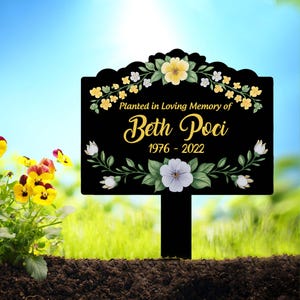 May include: Black garden stake with a floral design and the text "Planted in Loving Memory of Beth Poci 1976 - 2022".