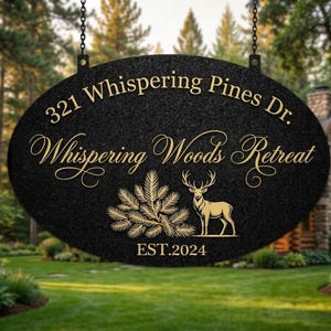 Könnte beinhalten: Schwarzes ovales Schild mit goldfarbenen Buchstaben und einer Hirschsilhouette. Auf dem Schild steht "321 Whispering Pines Dr. Whispering Woods Retreat" mit "EST.2024" unten. Das Schild hängt an Ketten vor einem verschwommenen Hintergrund im Freien.