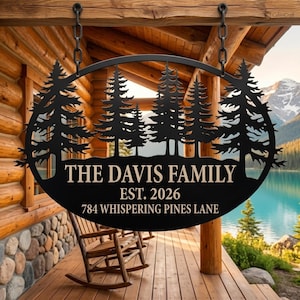 May include: Black metal family sign featuring a forest silhouette. The sign displays "THE DAVIS FAMILY EST. 2026 784 WHISPERING PINES LANE". It is suspended from a wooden structure, with rocking chairs visible.