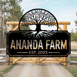 Pode incluir: Uma placa de metal preta com um design de árvore da vida e o texto "ANANDA FARM EST. 2023" pendurada em um portão de madeira.