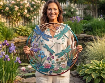 May include: A circular metal wall art piece featuring a colourful design of blue and teal dragonflies, purple iris flowers, and pink water lilies. The artwork includes cattails and green lily pads, all framed within a thin, gradient-coloured ring.