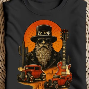 Op de afbeelding: Zwart t-shirt met een afbeelding van een bebaarde man met een hoge hoed en zonnebril, met de tekst "ZZ TOP". Het ontwerp bevat een rode hot rod, een gitaar en een woestijnlandschap met cactussen en een zonsondergang.