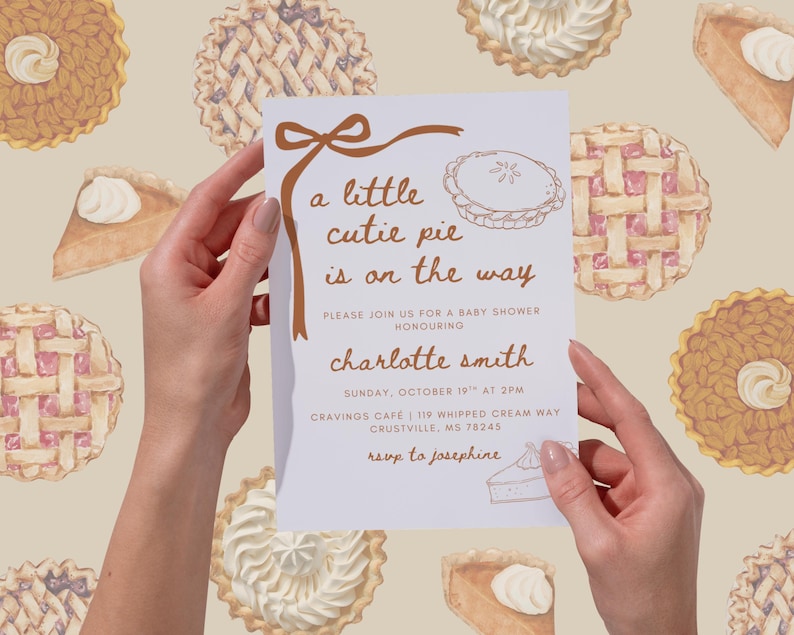 May include: A baby shower invitation held by hands, featuring the text "a little cutie pie is on the way." The invitation has a brown ribbon design and a pie illustration. The background has watercolor pie illustrations.