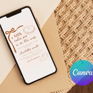 May include: A smartphone displays a baby shower invitation with the text "a little cutie pie is on the way." The invitation features brown illustrations of a pie and bow. The phone rests on a beige envelope and woven surface.