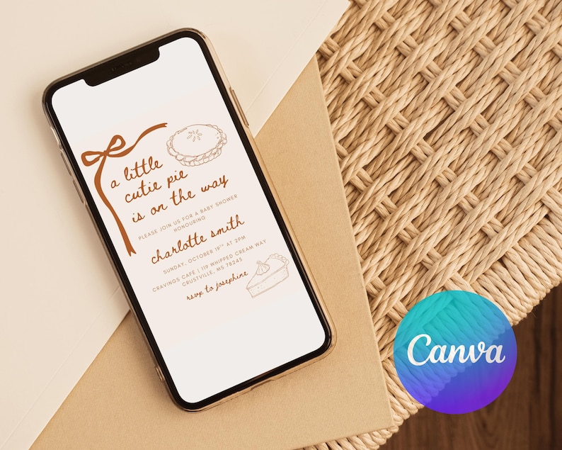 May include: A smartphone displays a baby shower invitation with the text "a little cutie pie is on the way." The invitation features brown illustrations of a pie and bow. The phone rests on a beige envelope and woven surface.