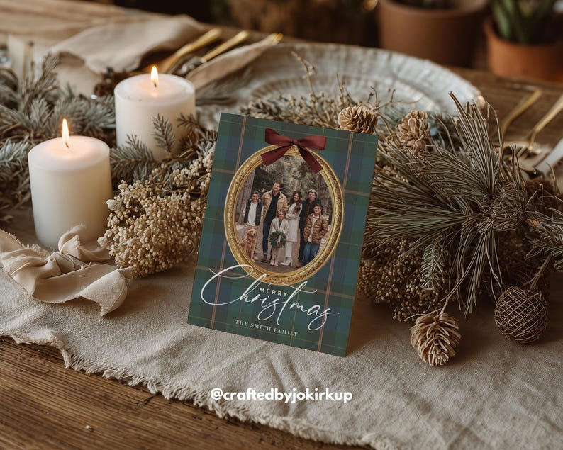 May include: A Christmas card with a family photo inside a gold frame, set against a green and blue plaid background. The card is adorned with a burgundy bow and the words "Merry Christmas" in elegant script. Two lit candles and festive greenery surround the card.