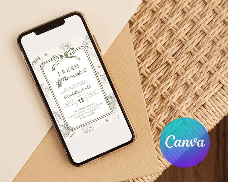 May include: A smartphone displays a digital invitation with the text "FRESH off the market." The invitation features a green border with illustrations of vegetables and flowers. The phone rests on a light brown surface next to a woven mat.