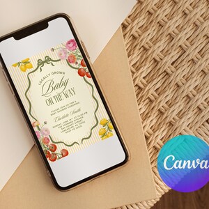 May include: A smartphone displays a baby shower invitation with floral and fruit illustrations. The invitation reads "Locally Grown Baby On The Way" with details for the event. The phone rests on a neutral surface, with a Canva logo in the corner.